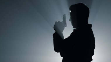 Siluet karanlıkta ateş etmeye odaklanmış bir adam. Tabancayla nişan alan suçlu.