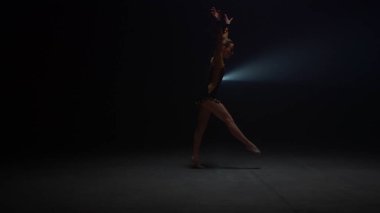 Atletik kadın karanlık stüdyoda amuda kalkıyor. İçeride esnek jimnastik eğitimi.