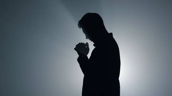 Silhouette ember Isten áldását kéri a sötétségben. Férfi személy imádkozik beltérben. — Stock Fotó