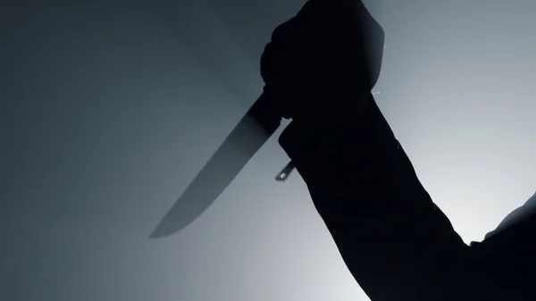 Silueta muže paži drží nůž ve tmě. Kriminální útok rukou s dýkou. — Stock fotografie