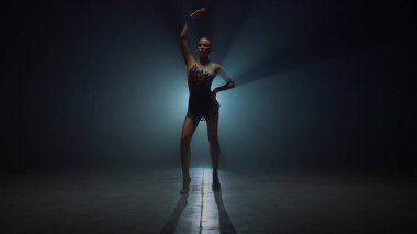 Jimnastikçi kız elini kaldırmış, karanlık bir yerde duruyor. Spor kadını içeride poz veriyor.. 