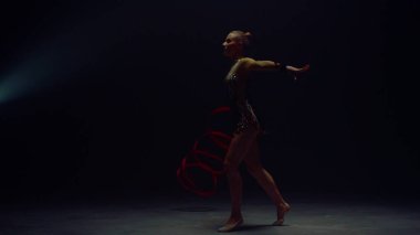 Jimnastik kurdelesiyle atlayan esnek bir kadın. Genç jimnastikçi içeride gösteri yapıyor..