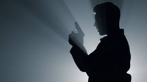 Silhouette offensore sparare pistola nel buio. Uomo concentrato che preme pistola grilletto — Foto Stock