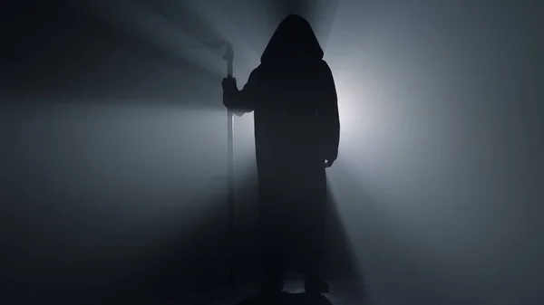 Silhouette scary scytheman standing in dark background. Grim reaper indoors.