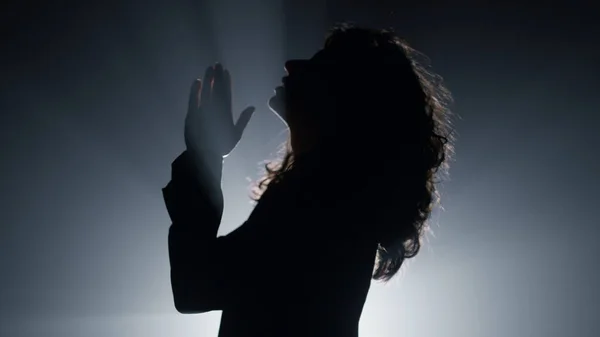 Silhouette woman praying in darkness. Believer girl whispering prayer indoors. — Stock Photo, Image