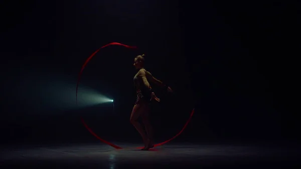 Mujer flexible girando la mano con cinta. Deportiva bailando en el espacio oscuro. — Foto de Stock