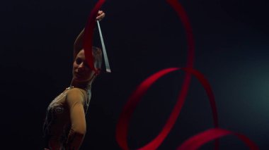 Ritmik jimnastikçi içeride kurdeleyle egzersiz yapıyor. Uçan bant ile poz veren kız.