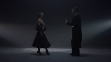 Karanlık sahnede el ele tutuşan çift. Erkek, kadını içeri davet eder..