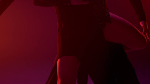 Unknown sensual woman lifting leg on dance partner indoors. Unrecognizable ballroom couple embracing inside. Passionate man and woman dancing in red light background.