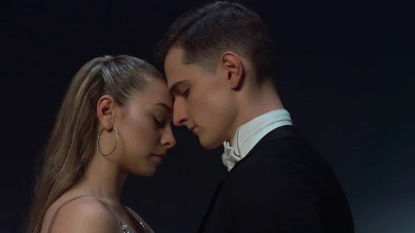 Ballroom couple standing in dark background. Young dancers looking each other.