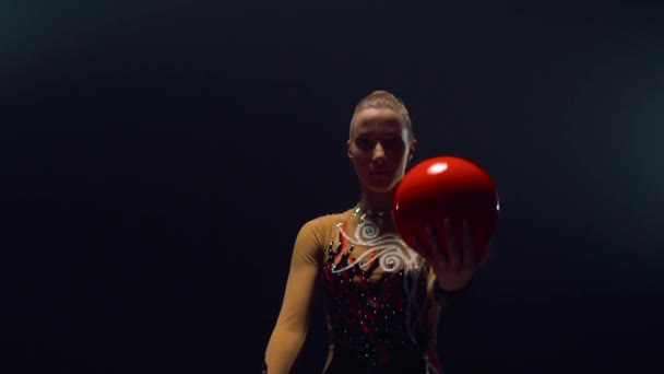 Genadig meisje rollende bal op handen binnen. Gymnastiektraining in de donkere ruimte. — Stockvideo