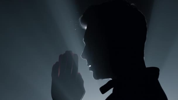 Ο άνθρωπος της σιλουέτας προσεύχεται στο σκοτάδι. Άντρας ψιθυρίζει προσευχή σε εσωτερικούς χώρους. — Αρχείο Βίντεο