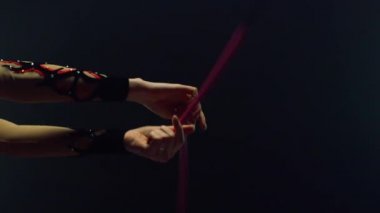 Kadın elleri kapalı alanda topuz büküyor. Jimnastikçi kolları teçhizatla egzersiz yapıyor.