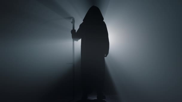 Silhouette grim Reaper áll otthon. Halál kaszás rivaldafényes háttérrel. — Stock videók