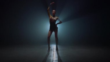 Jimnastikçi kız elini kaldırmış, karanlık bir yerde duruyor. Spor kadını içeride poz veriyor.. 