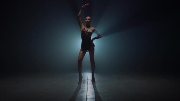 체조 스타 여자 애가 어두운 공간에 손을 들고 서 있어. 실내에 몸치장을 하는 향수병. — 비디오