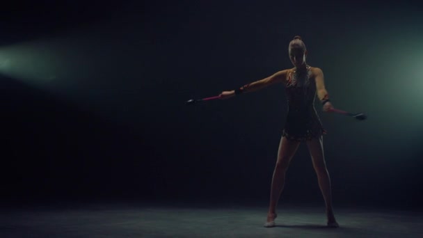 Elegante gimnasta haciendo ejercicio con el equipo en el interior. Mujer actuando con mazas — Vídeo de stock