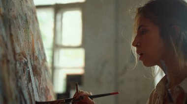 İş yerinde ciddi kadın resimleri. Kapalı alanda yağlı boya kullanan odaklanmış bir ressam..