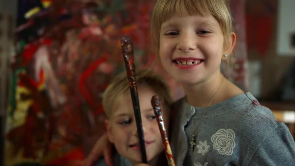Joyeux garçon mettant pinceau au nez dans un studio d'art. Sœur heureuse regardant à la caméra. — Photo