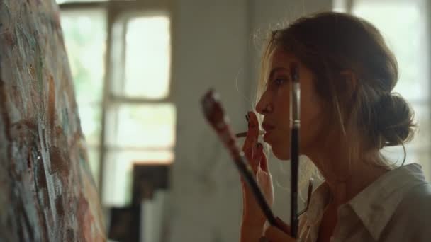 Tired woman smoking cigarette indoors. Serious painter holding paintbrushes. — Stock Video