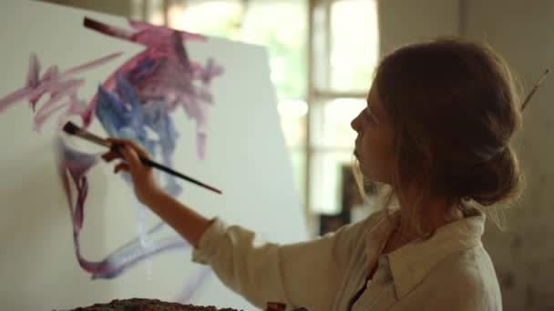 젊은 여성 예술가 가 스튜디오에서 그림을 그리고 있습니다. 실내에서 팔레트를 사용하는 숙련 된 화가. — 비디오