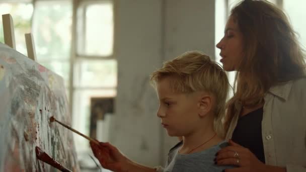 Ragazzo concentrato che disegna con insegnante al chiuso. Madre e figlio pittura in studio. — Video Stock