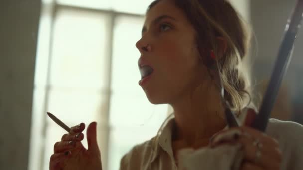 Kreativer Maler bläst Rauch im Atelier aus. Talentierte Mädchen rauchen drinnen. — Stockvideo