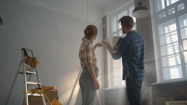 Familia joven alojada entre herramientas de construcción. Pareja elegir paredes color. — Vídeos de Stock