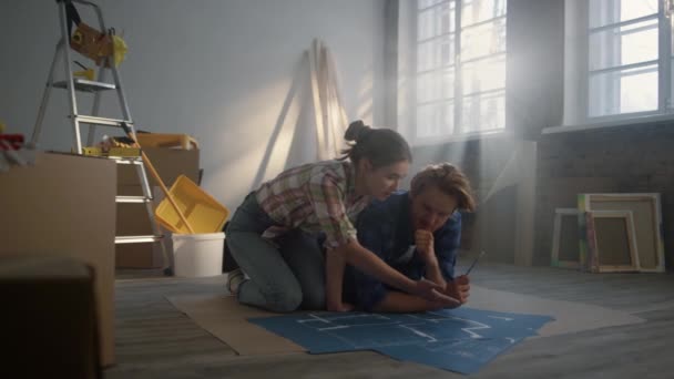 Konzentrierte Frau und junger Mann sprechen auf dem Fußboden über die Reparatur ihres Hauses. — Stockvideo