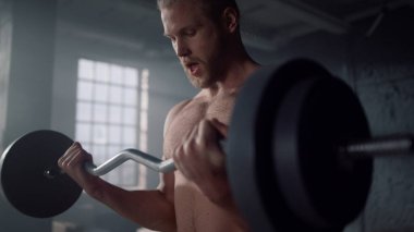 Gömleksiz adam kol egzersizi yapıyor. Sporcu halteri ağır ağırlıklarla kaldırıyor.