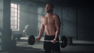 Spor kulübünde ağırlık kaldıran bir adam. Bağıran adam halterle kol egzersizi yapıyor.