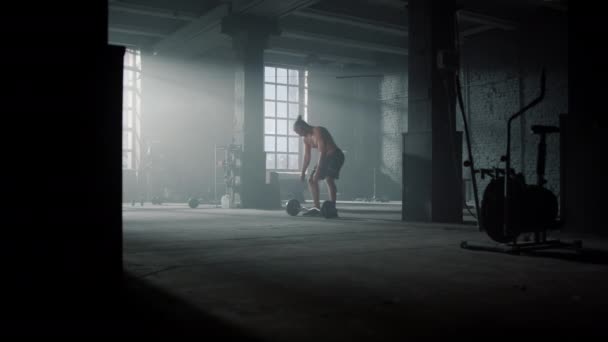 Chlápek stojící v tělocvičně se sportovním vybavením. Muž bere činku z podlahy — Stock video