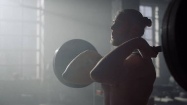 Adam halterle çömelme hareketi yapıyor. Ağır ağırlıklarla vücut geliştirme sporu 