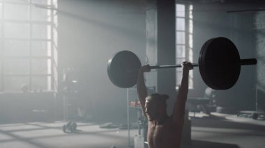 Adam halterle tepetaklak oturuyor. Güçlü sporcu ağırlık kaldırıyor. 