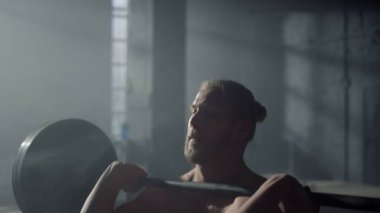 Güç toplayıcı antrenman sırasında ağırlık kaldırıyor. Ön koltukta halterle oturan adam.