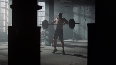 Powerlifter beden dersinde halter egzersizi yapıyor. Adam ön tarafta oturuyor. 