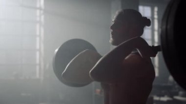 Adam halterle çömelme hareketi yapıyor. Ağır ağırlıklarla vücut geliştirme sporu 