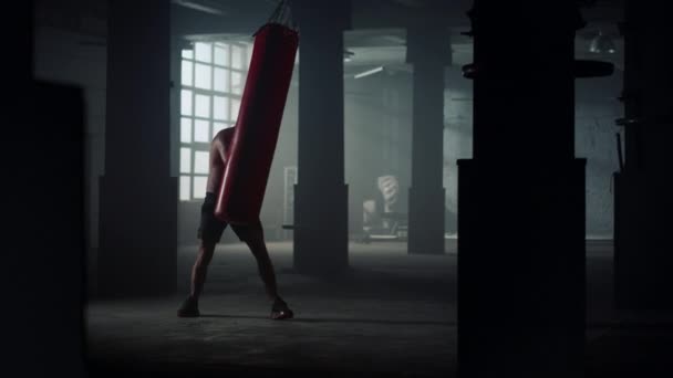 Fighter punching sports bag in loft building. Man kicking punch bag in gloves — Stock Video