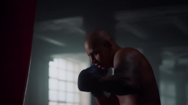 Dühös férfi üti a bokszzsákot. Sportolók edzése a sportklubban — Stock videók