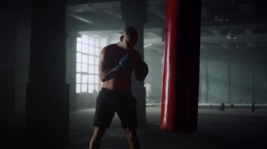 Boksör spor salonunda kum torbası üzerinde pratik yapıyor. Eldivenli boks çantası.