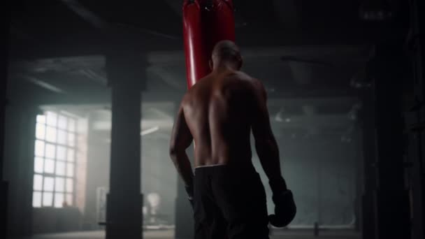 Boxeador masculino haciendo entrenamiento de intensidad en club deportivo. Afro hombre pateando saco de boxeo — Vídeo de stock