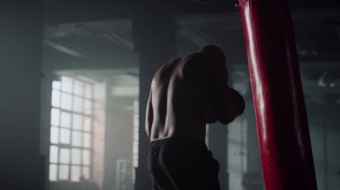 Boksör yoğun antrenman sırasında kum torbasına vuruyor. Spor salonunda adam kickboks yapıyor.