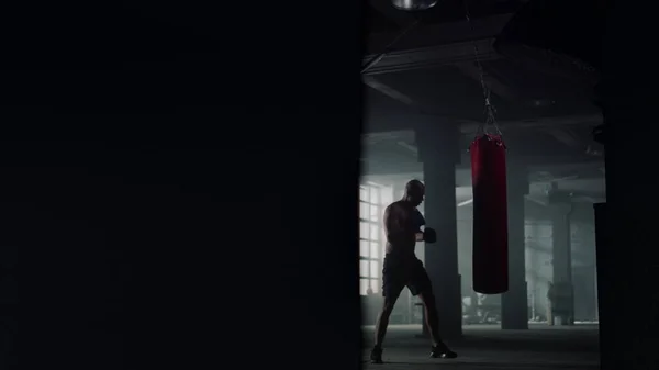 Hombre luchando con saco de boxeo. Chico en guantes de boxeo haciendo ejercicio de intensidad — Foto de Stock