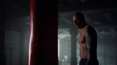 Spor kulübünde atletik adam kum torbasını yumrukluyor. Erkek boksör güç egzersizi yapıyor.