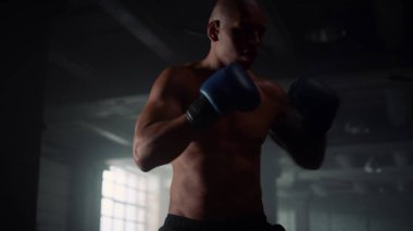 Çatı katında boks eğitimi alan bir adam. Erkek dövüşçü kum torbasını tekmeliyor 