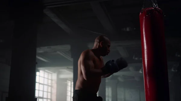 Boxeur mâle poinçonnage sac de sport dans le club de sport. Homme en colère coup de pied punch bag — Photo