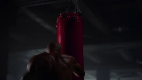 Un tipo fuerte saco de boxeo en el club deportivo. Boxeador masculino realizando ejercicio de fuerza —  Fotos de Stock