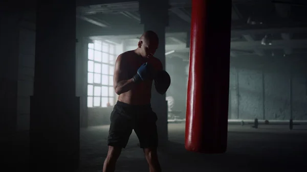 Boxer praticando chutes em saco de perfuração no ginásio. Guy boxe saco de esportes em luvas — Fotografia de Stock