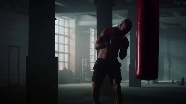 Un uomo che si allena a boxe in un club di combattimento. Boxer lotta con sacco da boxe — Foto Stock