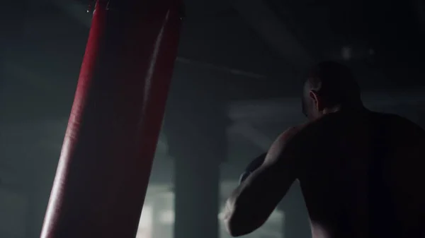 Hombre haciendo entrenamiento de boxeo en el club deportivo. Chico pateando saco de boxeo durante el entrenamiento — Foto de Stock